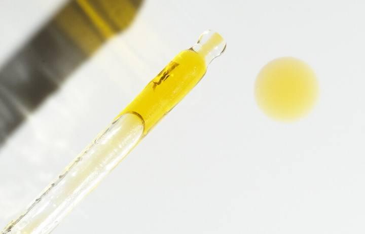 A close up shot of oil in a glass applicator, next to a drop of skin oil